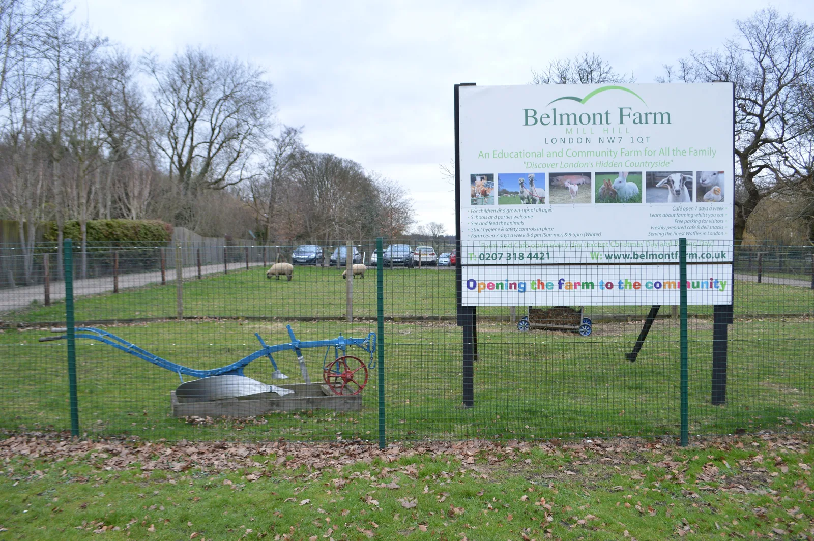 The sign at the entrance to Belmont Farm on The Ridgeway, Mill Hill, with sheep grazing in the paddock behind and an old plough in the foreground