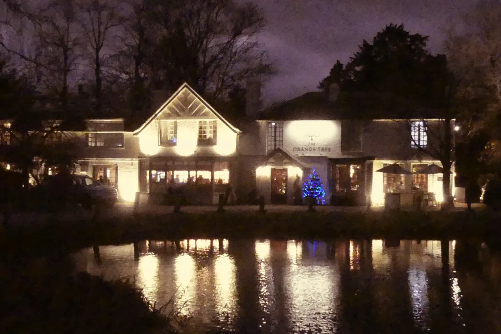 The Orange Tree in Totteridge village, lit up at night across the pond